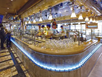 Eine helle Gelateria Amarillo an Bord der Costa Diadema mit mehreren Crew-Mitgliedern und Gästen, die Eis und Desserts auswählen. Der Tresen ist modern mit blauer LED-Beleuchtung gestaltet.