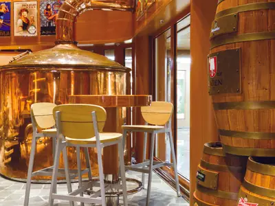 Blick in die Brauerei-Bar an Bord der Costa Diadema. Grosse, glänzende Kupferkessel, Holzhocker und Bartresen sowie gestapelte Bierfässer mit Logos sind sichtbar.