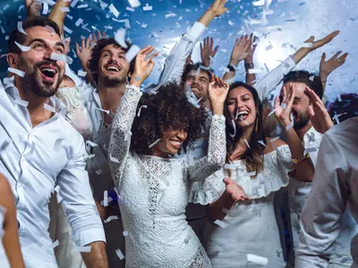 Eine Gruppe fröhlicher Menschen tanzt und lacht ausgelassen bei einer White Party mit Konfetti an Bord der Costa Diadema. Viele tragen weiße Kleidung.