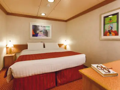 Geräumige Innenkabine der Costa Diadema mit Doppelbett, Nachttischen, Leuchten und zwei Kunstwerken an der Wand. Auf einem Beistelltisch liegen Buch und Brille bereit.