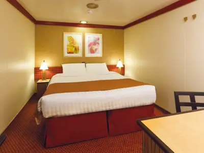 Eine gemütliche Innenkabine an Bord der Costa Diadema mit einem grossen Doppelbett, Nachttischen, Lampen und zwei farbigen Blumenbildern an der Wand. Der Raum ist mit warmen Farbtönen und einem roten Teppich gestaltet.