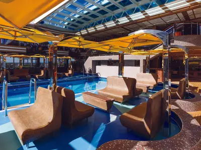 Der Lido Diana Poolbereich an Bord der Costa Diadema mit einem blauen Pool, beigen Loungemöbeln und gelben Sonnensegeln unter einem Glasdach.