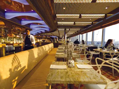 Das helle Restaurant Corona Blu an Bord der Costa Diadema. Gedeckte Tische, moderne Stühle, Kellner am Buffet und Gäste an den grossen Fenstern mit Stadtblick.