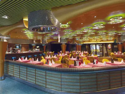 Ein bunt gestaltetes Restaurant an Bord der Costa Diadema mit rot-weiß karierten Tischdecken, gelben Stühlen und moderner Deckenbeleuchtung.