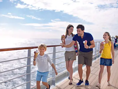 Eine lächelnde Familie, bestehend aus Eltern und zwei Kindern, geht mit Eiswaffeln über das Holzdeck der Costa Diadema. Im Hintergrund ist das Meer und ein blauer Himmel zu sehen.