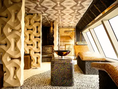 Innenansicht des modernen Samsara Spa an Bord der Costa Diadema mit goldenen Mosaikliegen, kunstvollen Säulen und einem hellen Fensterbereich.