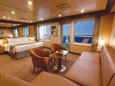 Helle Grand Suite der Costa Diadema mit großem Doppelbett, gemütlichem Sitzbereich und Balkon mit weitem Meerblick. Elegante Einrichtung, warmes Licht.