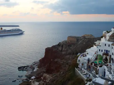 Blick auf die Costa Fascinosa auf dem blauen Meer vor den steilen, rötlichen Klippen und den weißen Häusern von Santorini in Griechenland.