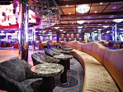 Sitzbereich der Grand Bar Topkapi an Bord der Costa Fascinosa mit runden Tischen, gemusterten Sesseln und einer geschwungenen Couch.