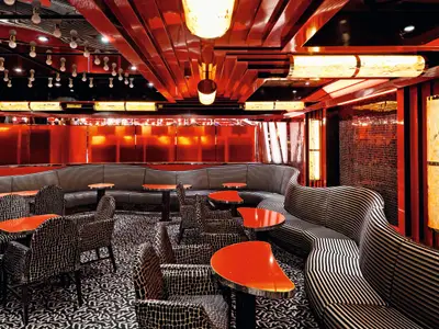 Eine elegant eingerichtete Lounge an Bord der Costa Fascinosa mit rot glänzenden Wänden, gestreiften Sofas und gemusterten Sesseln.