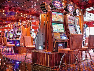 Blick auf moderne Spielautomaten mit davor stehenden, gemusterten Sesseln im Casino an Bord der Costa Fascinosa.