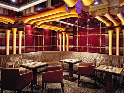 Gemütliche Lounge-Ecke in der Bar Classico Malia an Bord der Costa Fascinosa mit rot-goldener Dekoration und braunen Sesseln.