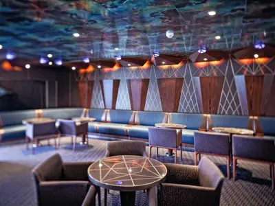 Blick in die stilvolle Cheri Lounge an Bord der Costa Fascinosa mit dunklen Sesseln, runden Tischen und markanter Wandgestaltung.