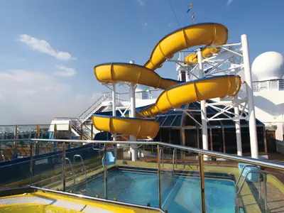 Blick auf die große gelbe Wasserrutsche und einen kleinen Pool auf dem Außendeck der Costa Fascinosa bei strahlendem Sonnenschein.