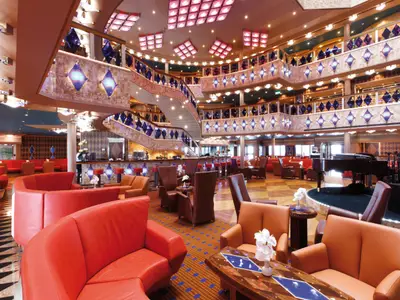 Das elegant beleuchtete Atrium an Bord der Costa Favolosa verfügt über mehrere Decks, rote Ledersessel, einen Flügel und blaue Dekoelemente.