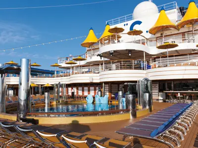 Sonnendeck an Bord der Costa Favolosa mit einem Pool, blauen Liegestühlen und markanten gelben, kegelförmigen Dächern bei Sonnenschein.