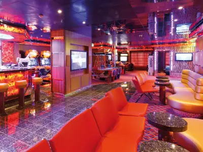 Ein bunt beleuchtetes Game Center mit roten Loungesesseln, Barhockern und Spielautomaten an Bord der Costa Favolosa.