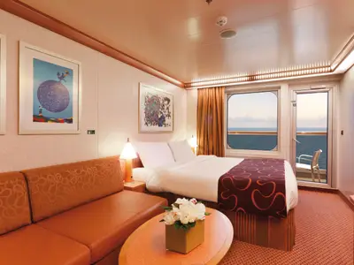 Blick in eine komfortable Balkonkabine an Bord der Costa Favolosa mit Doppelbett, Sofa und direktem Meerblick.