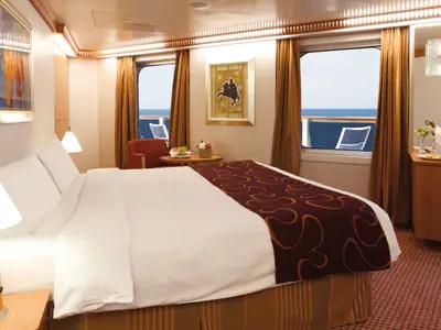 Eine luxuriös eingerichtete Suite mit großem Doppelbett, Sitzecke und Meerblick an Bord der Costa Favolosa.