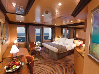 Geräumige Suite an Bord der Costa Favolosa mit einem Doppelbett, Sitzecke und Balkon mit Blick auf das blaue Meer.