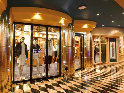 Blick in die glänzende Shopping-Passage an Bord der Costa Favolosa mit Schaufenstern und goldenen Säulen.