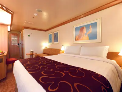 Innenansicht einer gemütlichen Kabine an Bord der Costa Favolosa mit einem großen Doppelbett, warmem Licht und einem Sofa im Hintergrund.