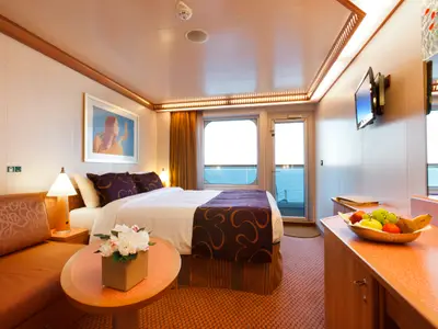 Doppelbett, Sofa und Obstschale in einer hellen Balkonkabine mit Meerblick an Bord der Costa Favolosa.