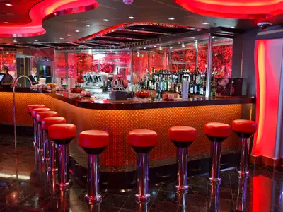 Die moderne Piano-Bar Camelot an Bord der Costa Favolosa besticht durch eine beleuchtete Theke mit roten Barhockern und glänzenden Chromfüßen.