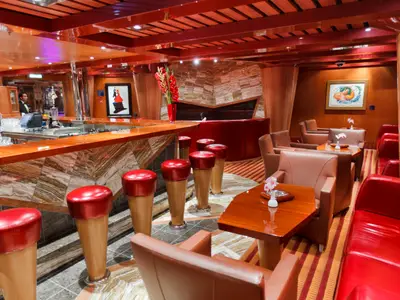 Elegante Bar Classico Montespan an Bord der Costa Favolosa mit roten Barhockern, Ledersesseln und warmen Holztönen.