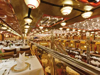Ein prachtvolles mehrstöckiges Restaurant an Bord der Costa Favolosa mit goldenen Deckenleuchten und elegant gedeckten Tischen.