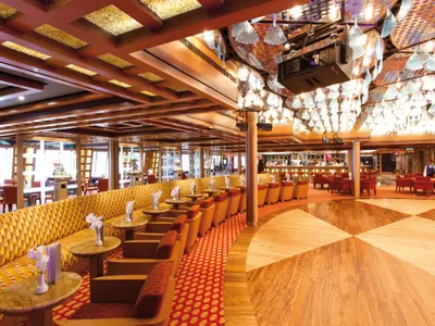 Die Grand Bar Palatino an Bord der Costa Favolosa mit hölzerner Tanzfläche, geschwungenen gelben Sofas und glitzernder Lichtinstallation.