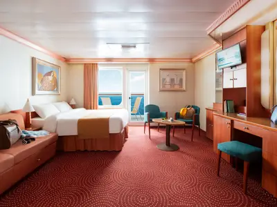 Helle Balkonkabine der Costa Fortuna mit Doppelbett, Sofa, Schreibtisch, Sitzbereich und privatem Balkon mit Meerblick. Roter Teppich mit Muster.