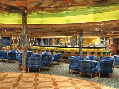 Die Grand Bar Conte di Savoia an Bord der Costa Fortuna. Blaue Plaid-Sessel, beleuchtete Bar, kunstvolle Deckenmalerei und bunte Säulen. Einladendes Interieur in Abendstimmung, ohne Personen.