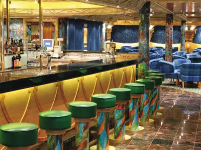 Der farbenfrohe Bar- und Loungebereich Grand Bar Conte di Savoia 1932 an Bord der Costa Fortuna mit grünen Barhockern, einer langen Theke, Flaschen und Gläsern, sowie blauen Sesseln im Hintergrund.