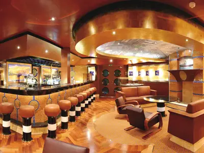 Panoramablick in die stilvolle Cigar Bar Classico Roma 1926 an Bord der Costa Fortuna mit langer Bar, braunen Hockern und Leder-Sitzgruppen in warmen Gold- und Brauntönen. Holzboden und kunstvolle Deckenbeleuchtung prägen den Raum.