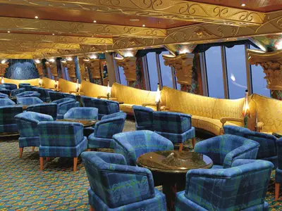 Elegante Bar-Lounge an Bord der Costa Fortuna. Viele blaue Sessel, gelbe Sofas und Tische gruppieren sich. Goldene Decken- und Säulenverzierungen. Große Fenster mit Meerblick.