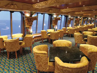Elegante Lounge an Bord der Costa Fortuna mit gold-gemusterten Sesseln, dunklen Tischen und Ausblick auf das weite Meer.