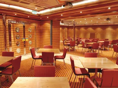 Ein leerer Konferenzraum an Bord der Costa Fortuna mit zahlreichen Holztischen und roten Stühlen, umgeben von holzvertäfelten Wänden und Teppichboden in warmen Farben.