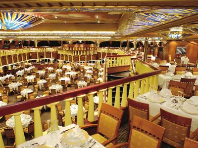 Elegantes Restaurant Michelangelo an Bord der Costa Fortuna. Mehrere Ebenen, festlich gedeckte Tische und goldene Geländer dominieren den luxuriösen Raum.