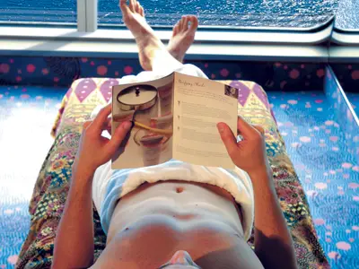 Eine Person liegt entspannt auf einer gemusterten Liege an Bord der Costa Fortuna und liest eine Spa-Broschüre über Reinigungsmasken. Im Hintergrund sind die Füsse der Person zu sehen.
