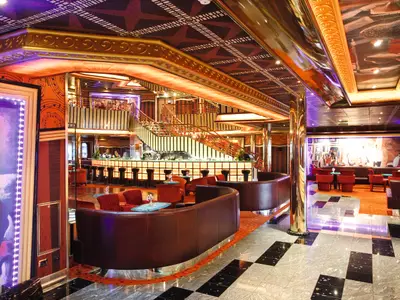 Das prunkvolle, in warmen Tönen beleuchtete Atrium an Bord der Costa Pacifica mit einer Bar, bequemen Ledersesseln und einer eleganten Treppe.