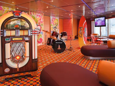 Ein farbenfroher Teen-Bereich an Bord der Costa Pacifica mit Retro-Jukebox, Schlagzeug, buntem Teppich und gemütlichen Sitzgelegenheiten.