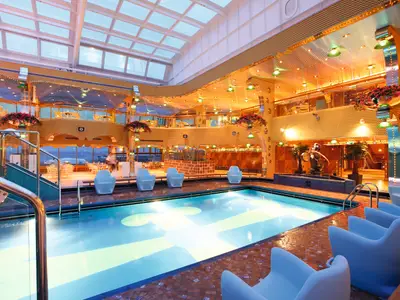 Blick auf den überdachten Calypso-Pool an Bord der Costa Pacifica mit blauen Sesseln und goldener Decke unter einem Glasdach.