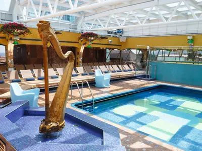 Der Lido Ipanema Poolbereich an Bord der Costa Pacifica mit einer goldenen Harfenskulptur, Liegestühlen und einem Pool unter einem Glasdach.