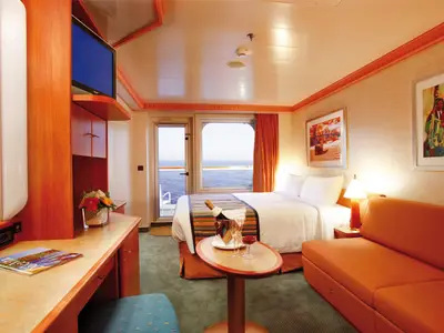 Innenansicht einer gemütlichen Balkonkabine an Bord der Costa Pacifica mit Doppelbett, Couch, Champagnerkübel und Blick auf das Meer.