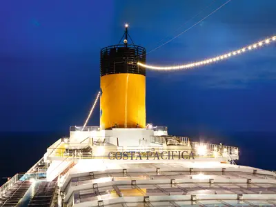 Der beleuchtete gelbe Schornstein der Costa Pacifica ragt in den nächtlichen Himmel über dem Meer.