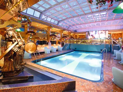 Der überdachte Poolbereich Lido Calypso an Bord der Costa Pacifica mit einer bronzenen Skulptur im Vordergrund und blau beleuchtetem Pool.