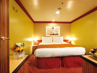 Eine gemütlich eingerichtete Innenkabine an Bord der Costa Pacifica mit Doppelbett, Blumenschmuck und warmen Gelbtönen.