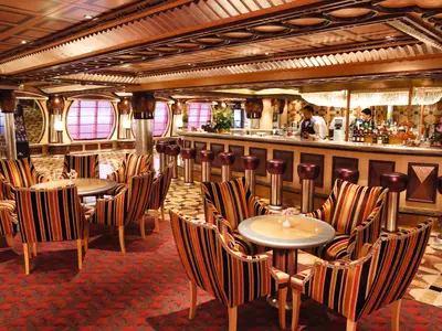 Die stilvolle Grand Bar Rhapsody an Bord der Costa Pacifica mit bunt gestreiften Sesseln und Barhockern.