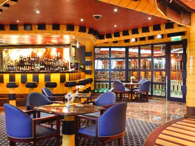 Rick's Piano Bar an Bord der Costa Pacifica mit blauen Sesseln, eleganten Holztischen und einer gut sortierten Bar im Hintergrund.